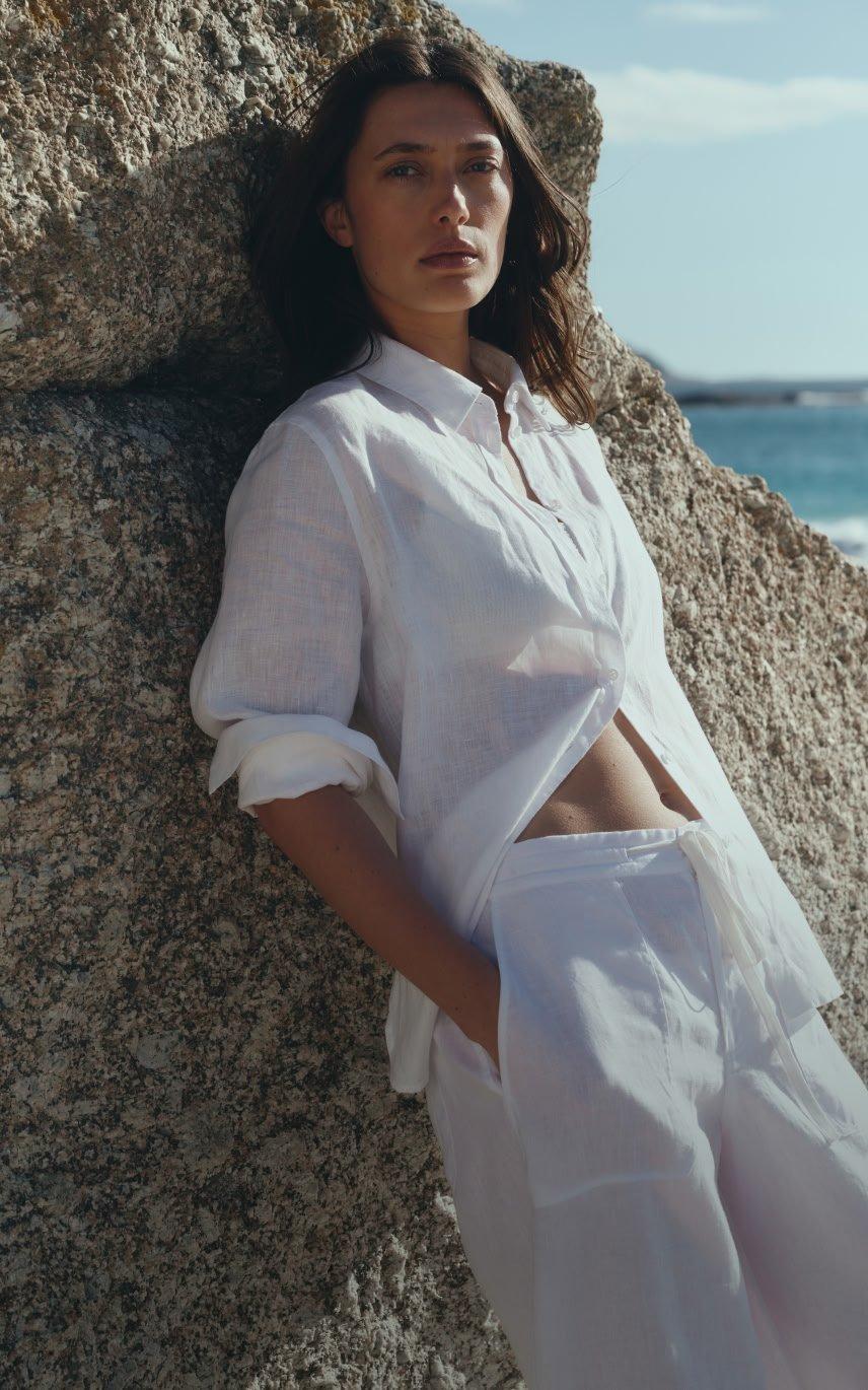 a woman in white jumpsuit standing on beach with bag