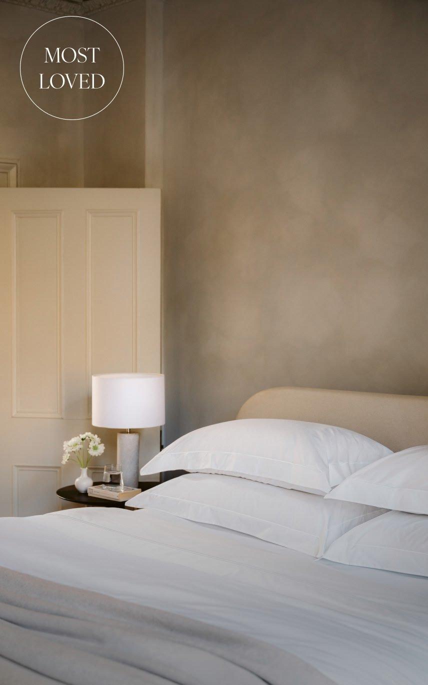 a bed with white sheets and pillows on a nightstand