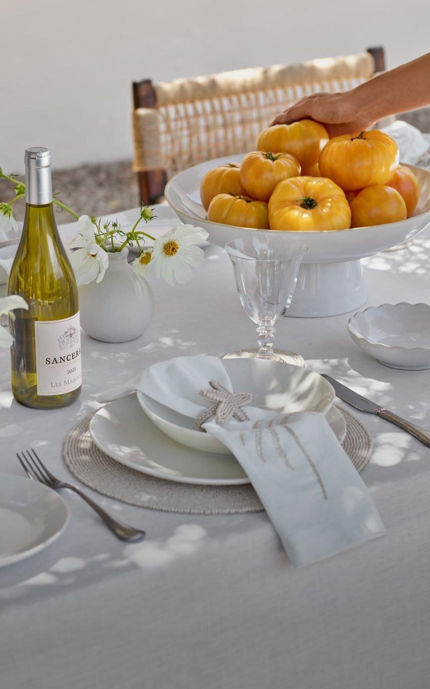 a table setting with a white plate, white bowl, white wine glass, white napkin,