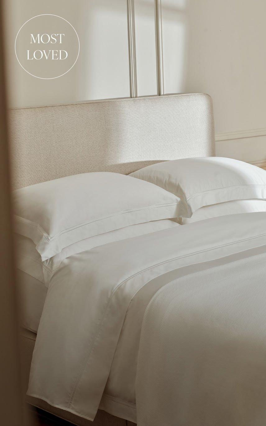 a bed with white sheets and pillows in a bedroom