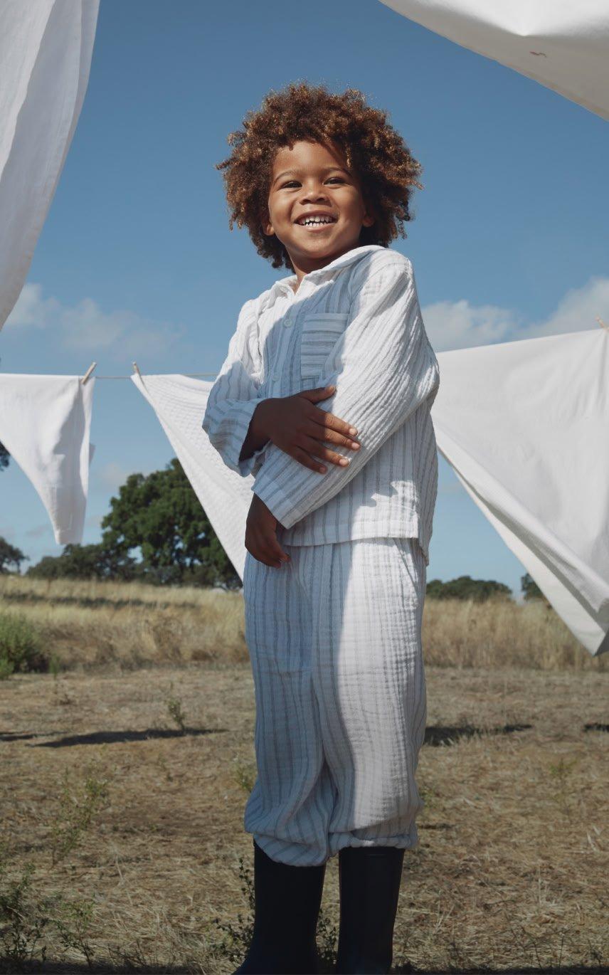 a young boy smiling while standing in front of a line of clothes