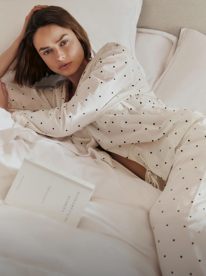 a woman laying on a bed in a white polka dot dress