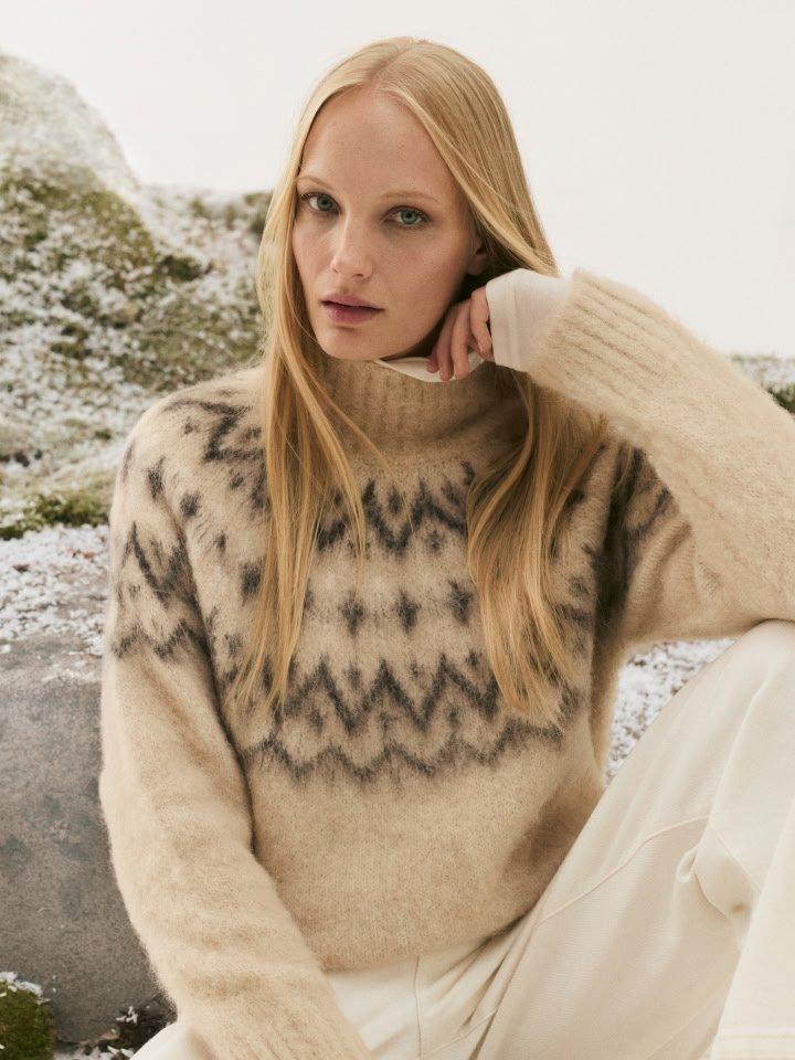 a woman in a sweater and pants sitting on a rock