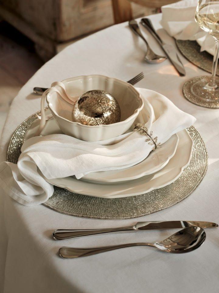 a white table setting with silverware and a bowl of fruit