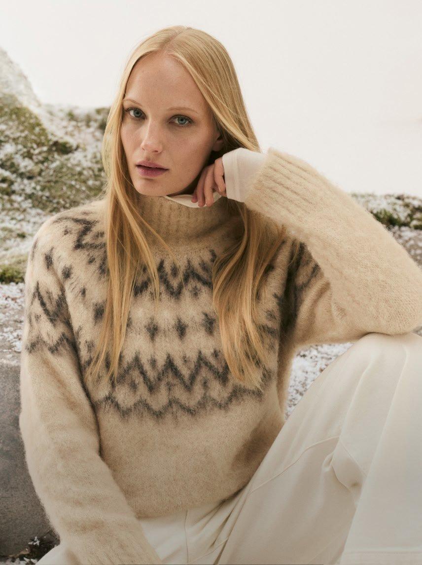 a woman in a sweater and pants sitting on a rock