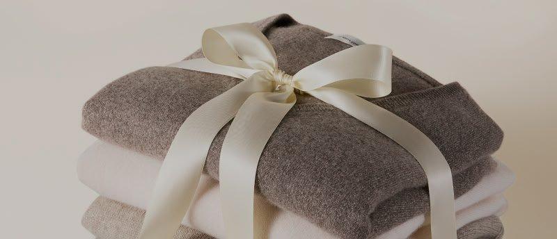 a stack of four sweaters with a ribbon tied around them