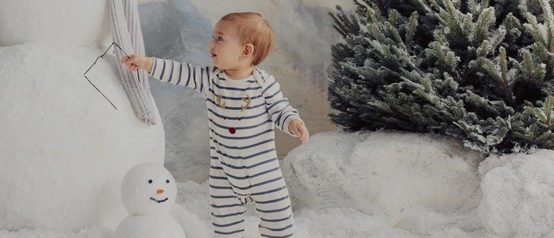 a baby in striped pajamas standing next to a snowman