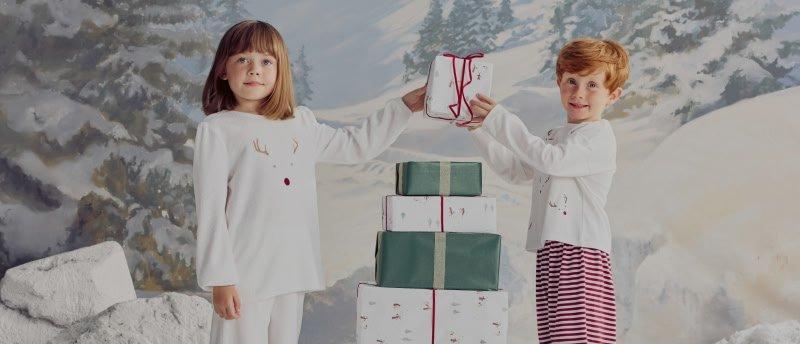 two children standing on a sled with presents in the snow