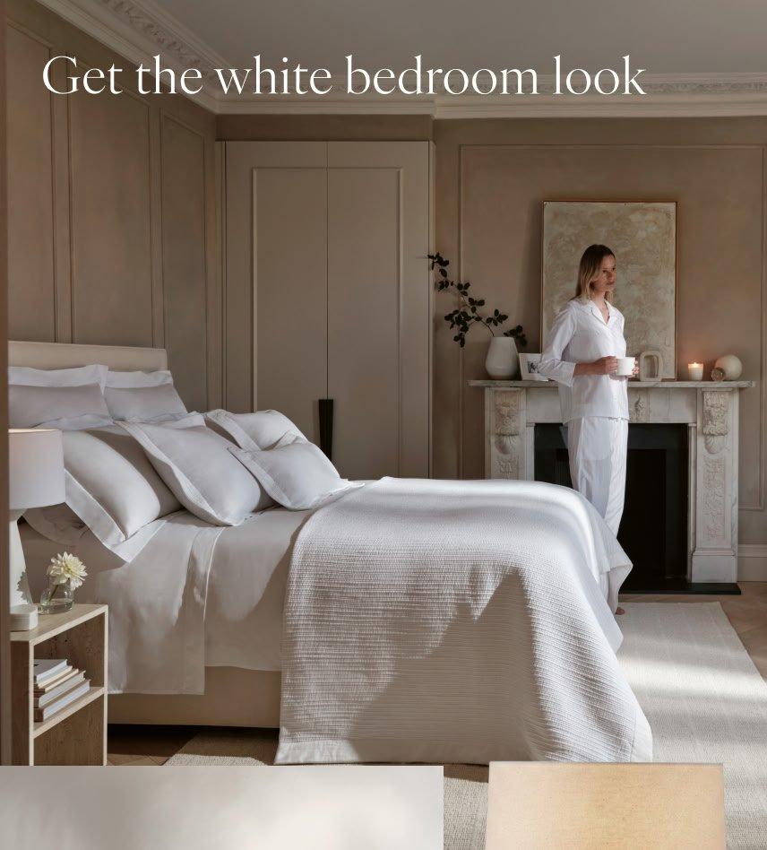 a woman standing in a bedroom with a white bed and white pillows