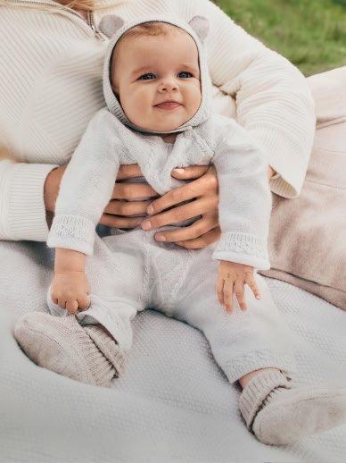 a woman holding a baby in a white outfit on a blanket