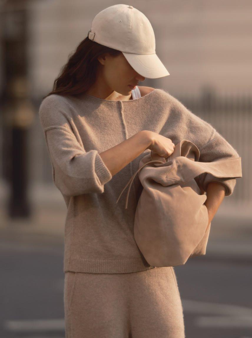 a woman in a hat and sweater holding a bag on the street