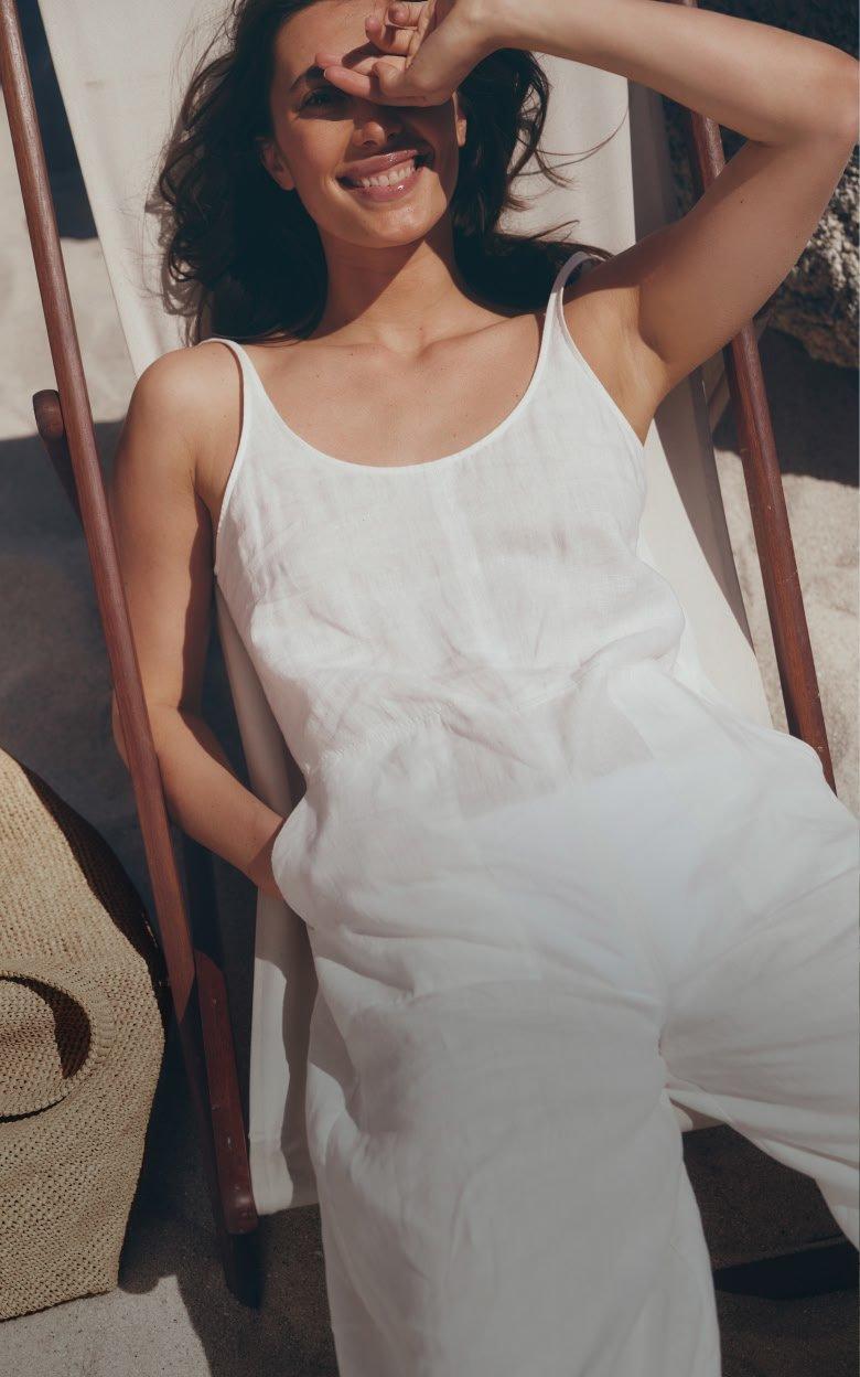 a woman in white jumpsuit sitting in a chair on a beach