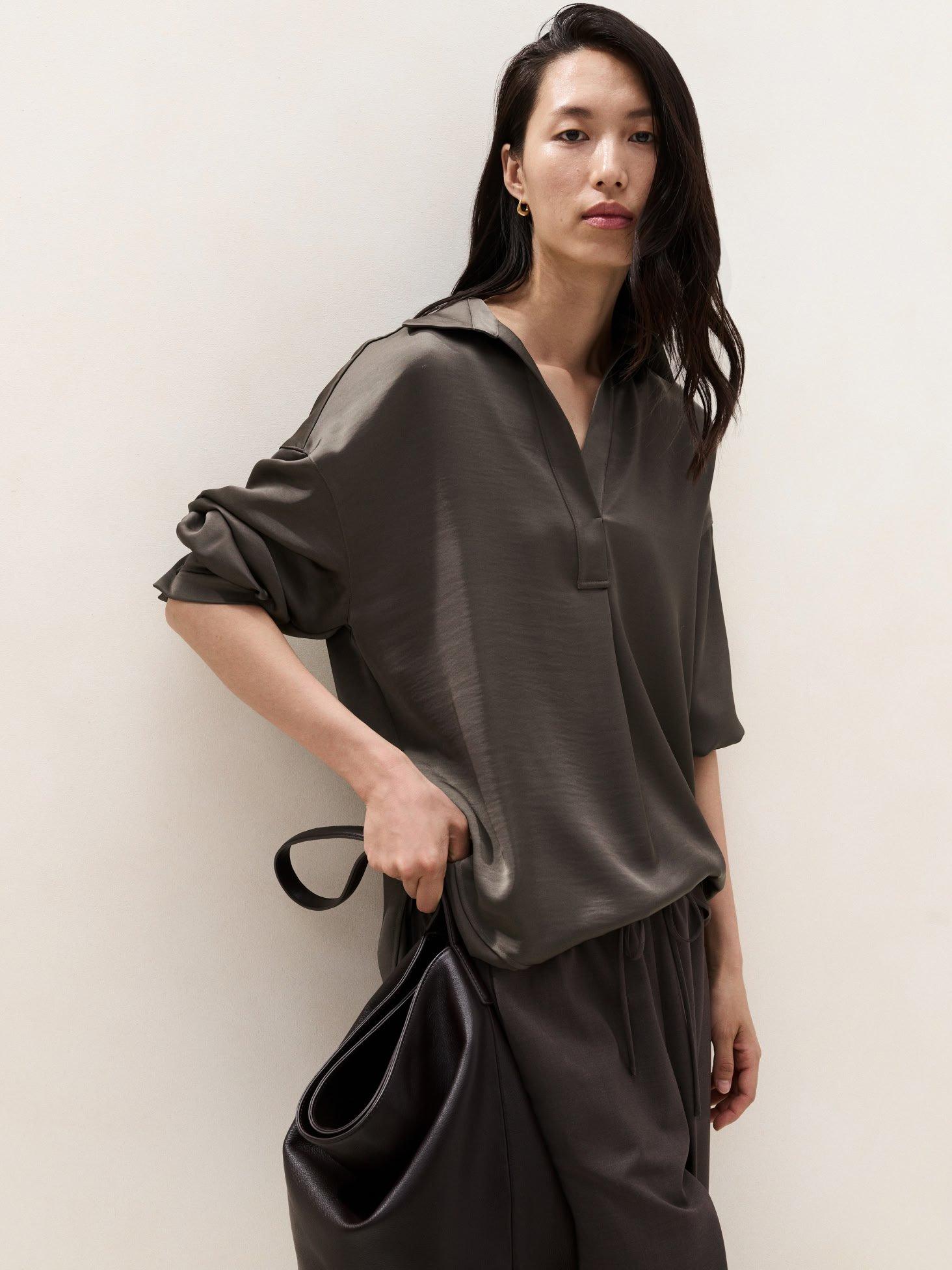 a woman in a grey shirt and pants holding a black bag