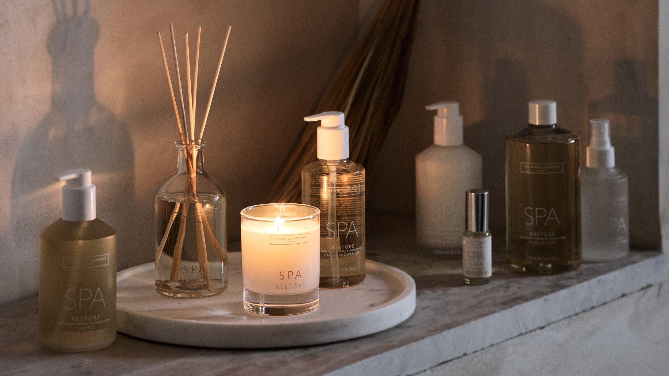 a candle and a few bottles of lotion sit on a shelf