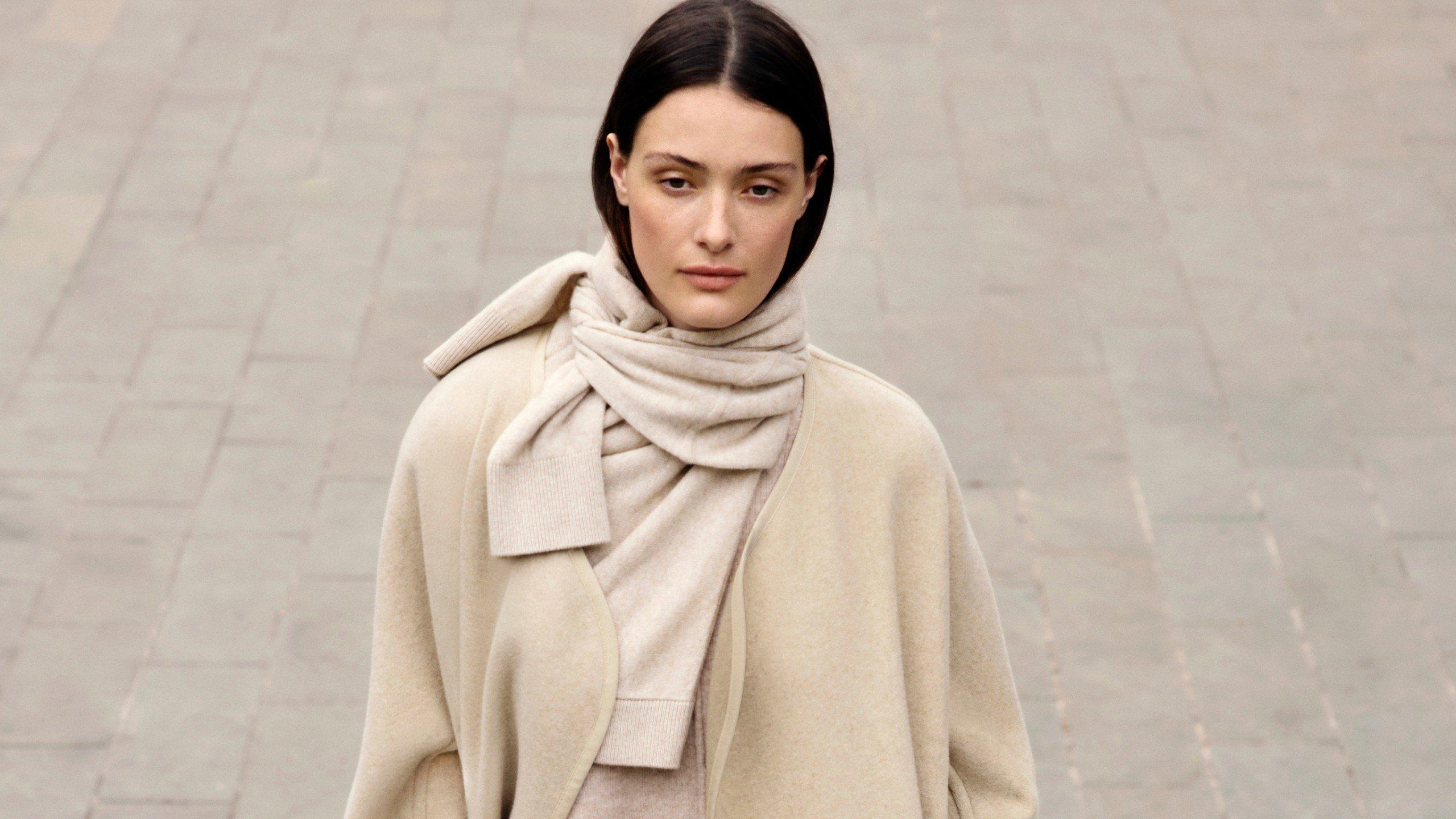 a woman in a white coat and scarf walking down a street