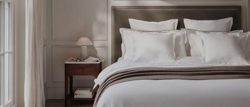 a bed with white sheets and pillows in a bedroom