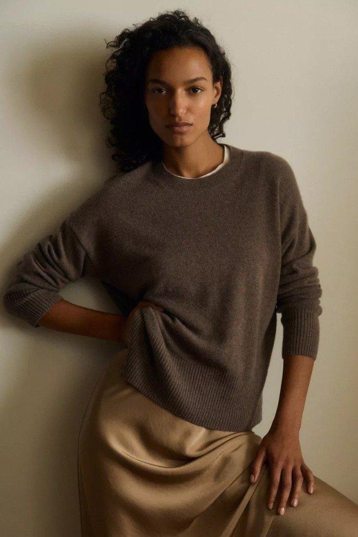 a woman in a brown sweater leaning against a wall