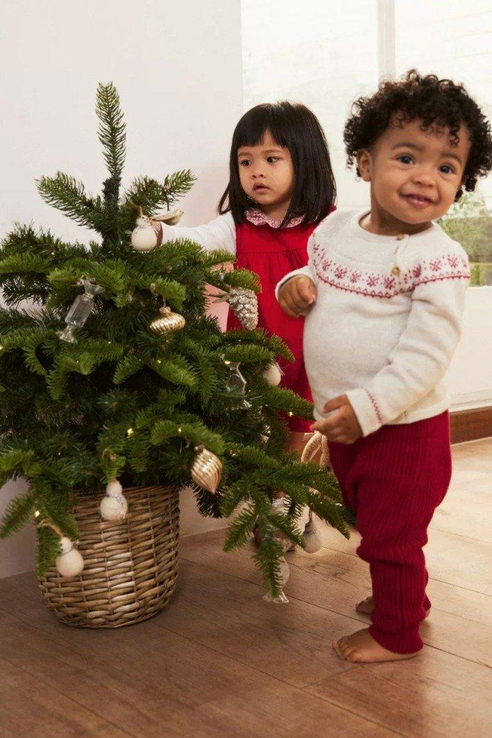 two children standing next to a small christmas tree in a room