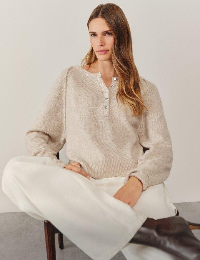 a woman in a beige sweater and brown boots sitting on a chair