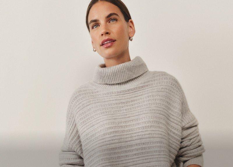 a woman in a grey turtle neck sweater and white pants