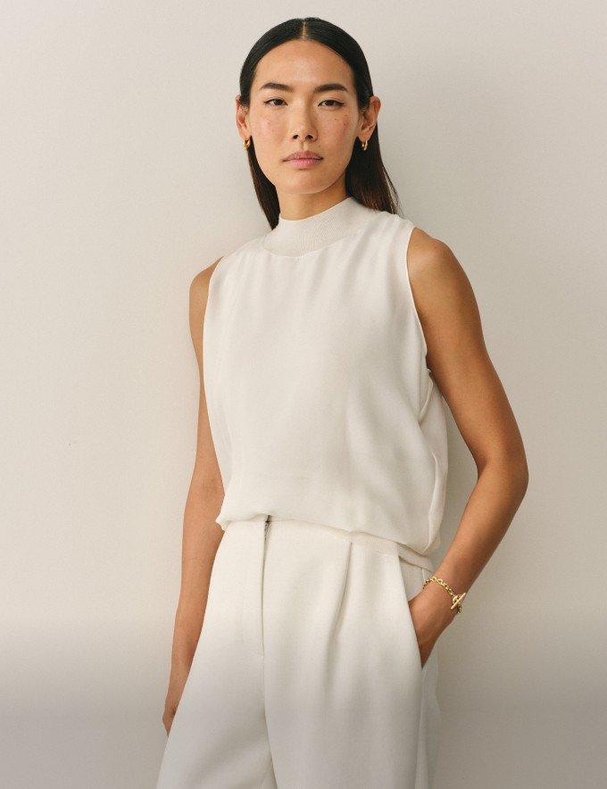 a woman in a white top and pants standing against a wall