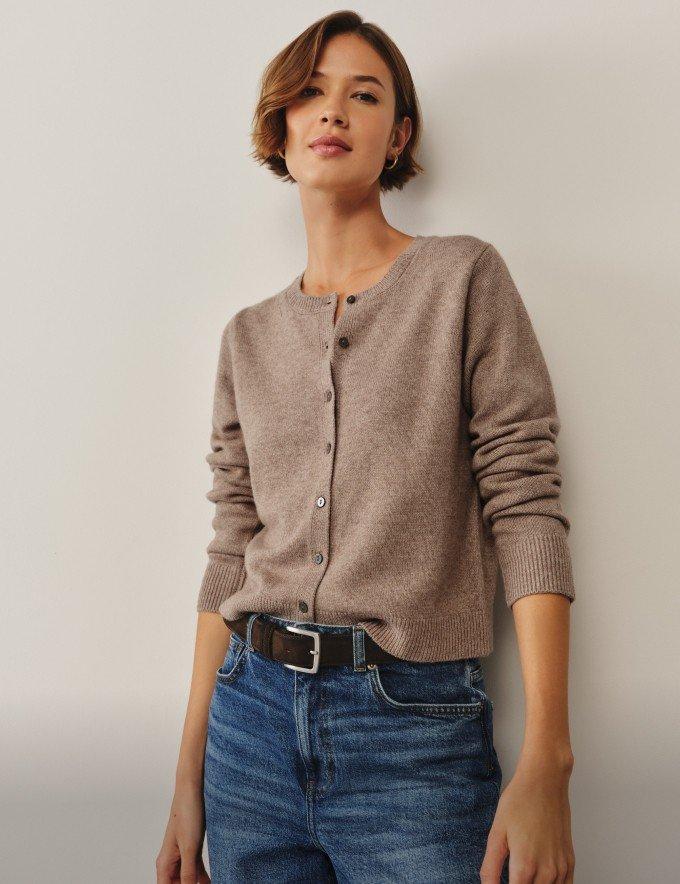 a woman in jeans and a sweater is leaning against a wall