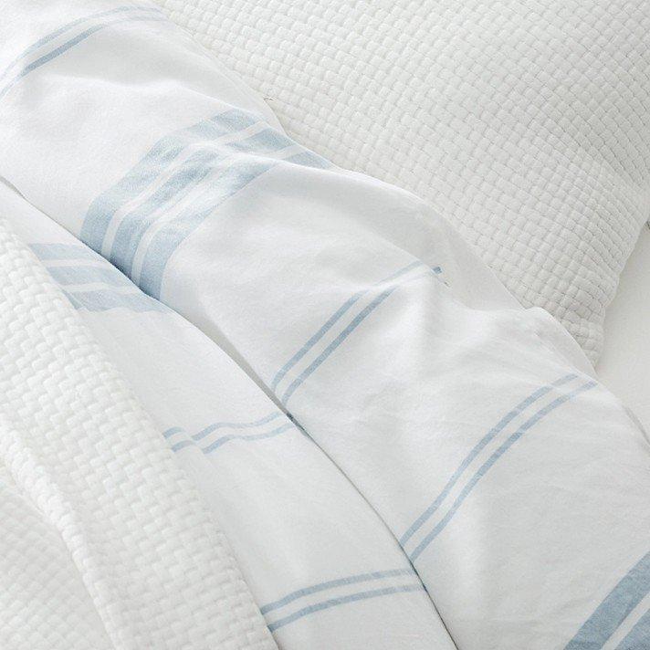 a close up of a white bed with blue and white striped sheets