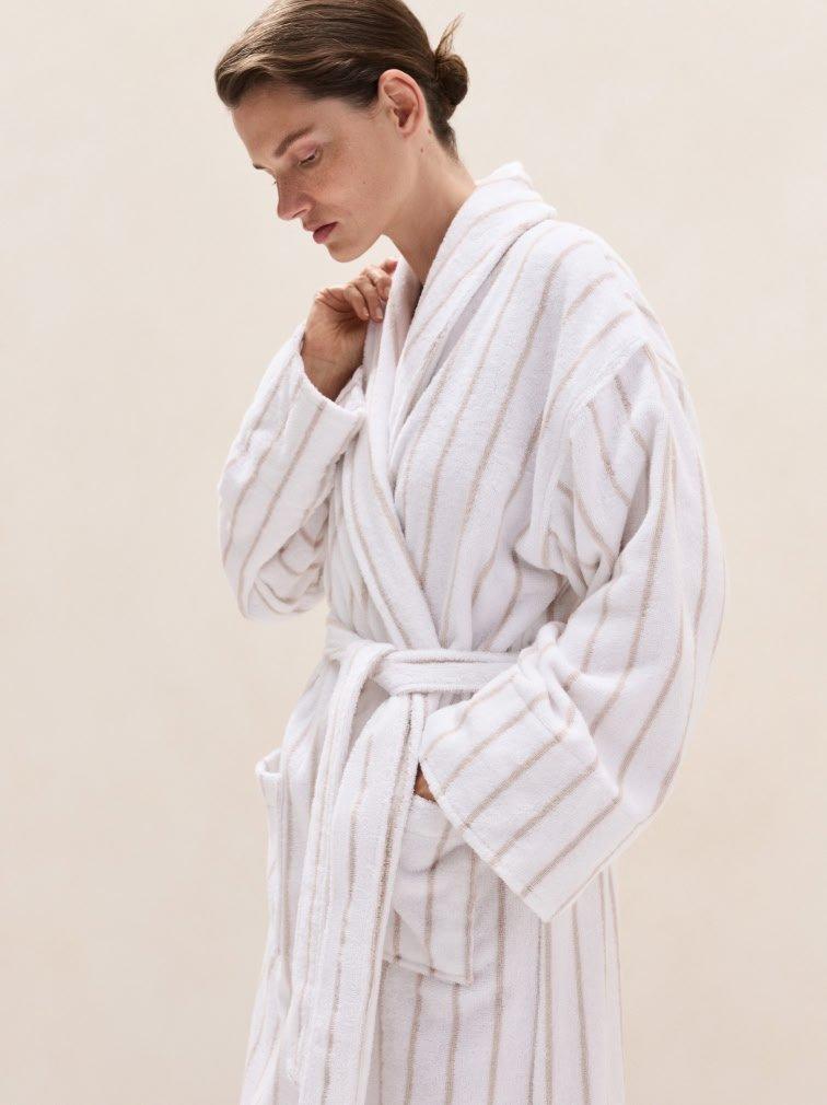 a woman in a white robe standing against a wall