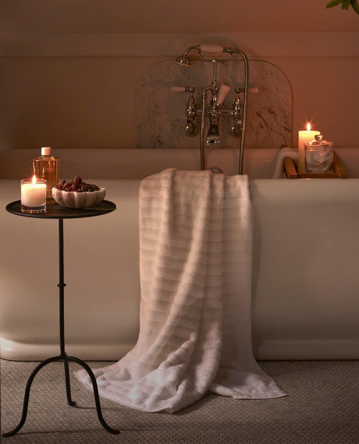 a bathtub with candles lit on a table next to it