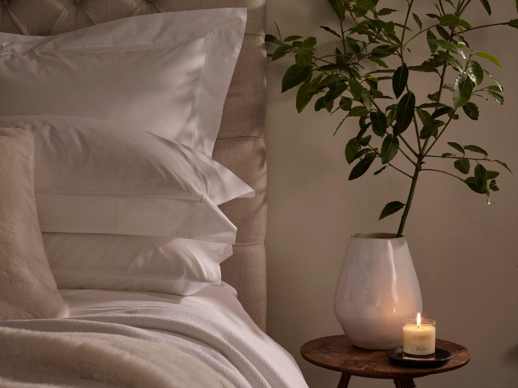 a candle on a small table next to a bed with a white pillow