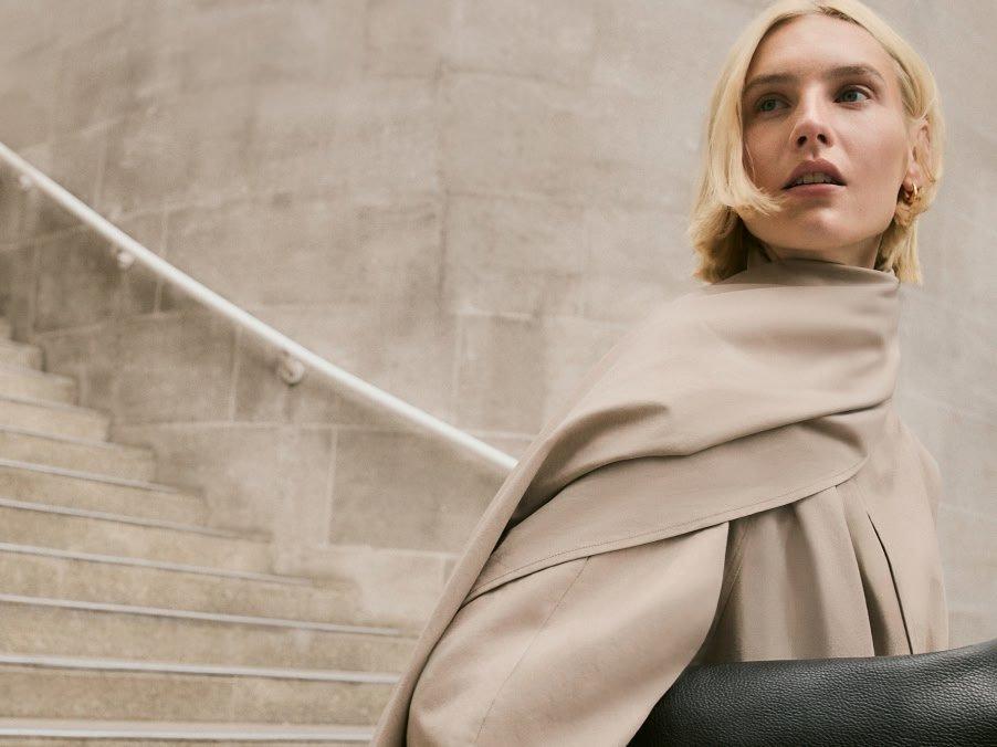 a woman in a beige coat walking down a set of stairs