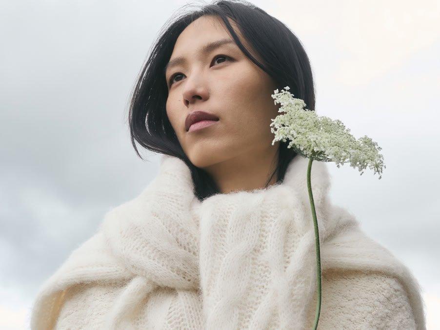 a woman in a white sweater holding a flower in her hand