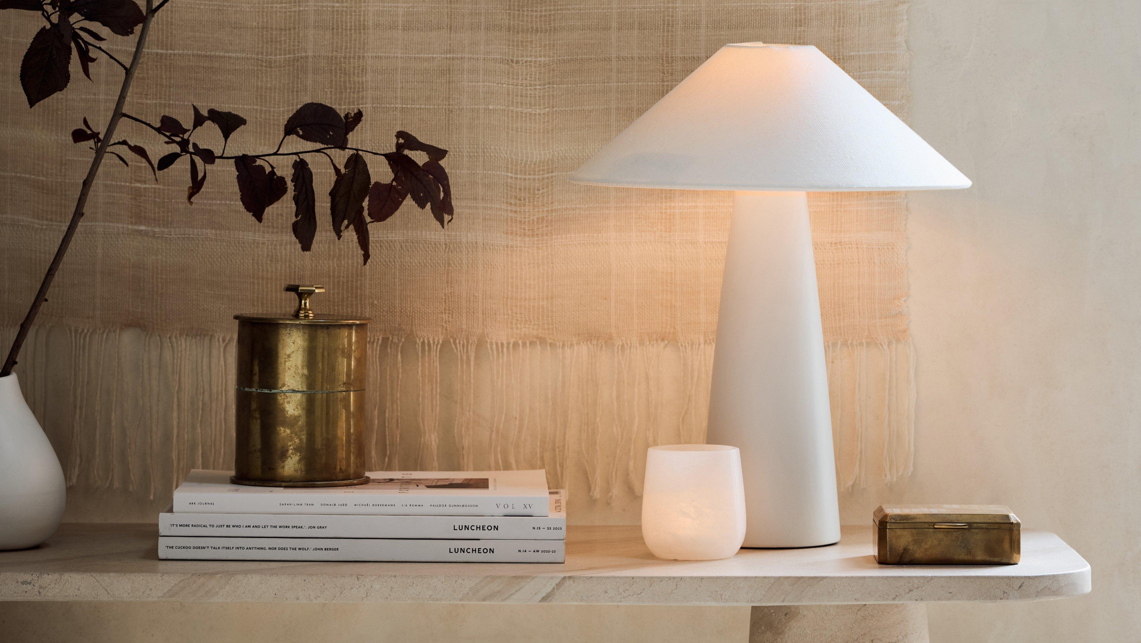 white lamp on a table next to books and a plant