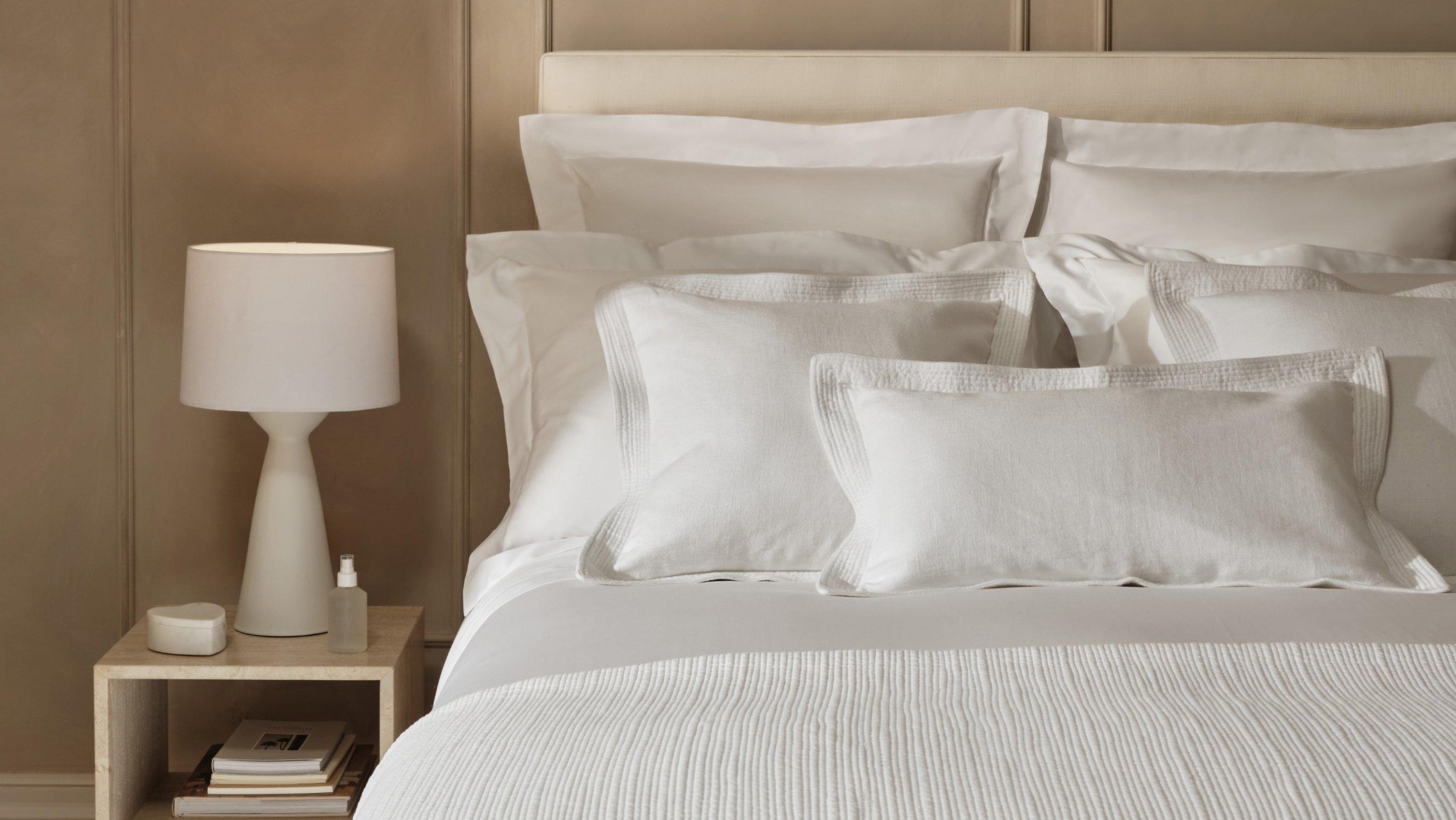 white lamp on a table next to a bed 