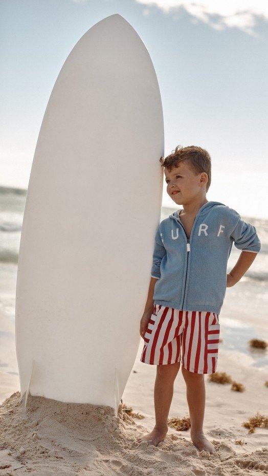 a young boy walking on the beach with a surfboard