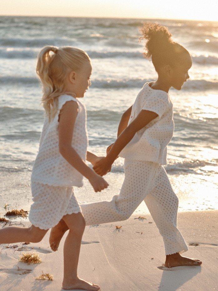 two children standing on a sandy hill with a rainbow in the sky