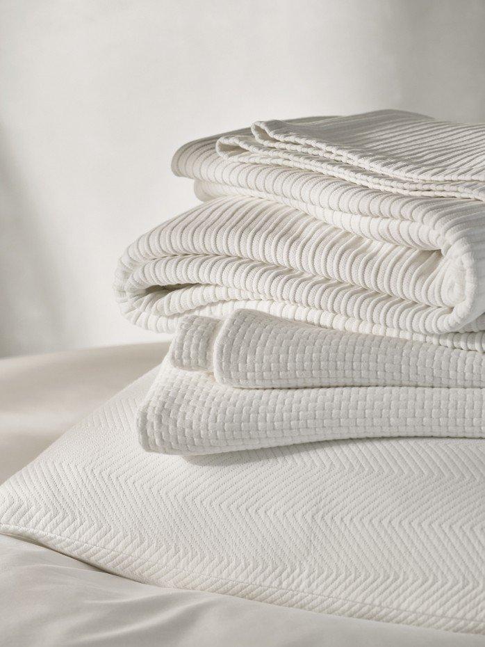 a stack of white towels on a bed with a white pillow