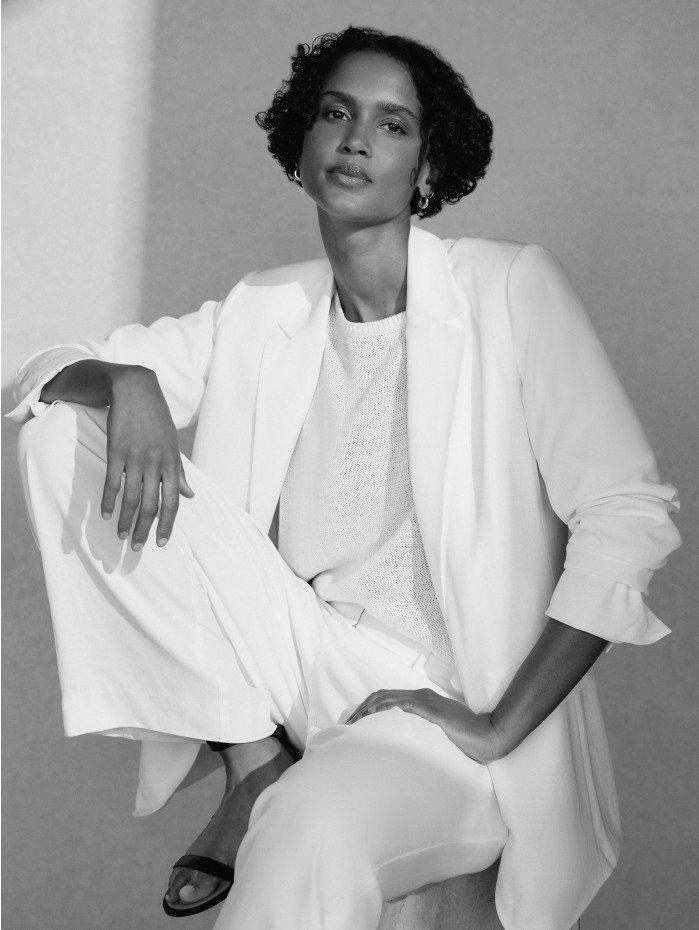 a woman in a white suit sitting on a stool