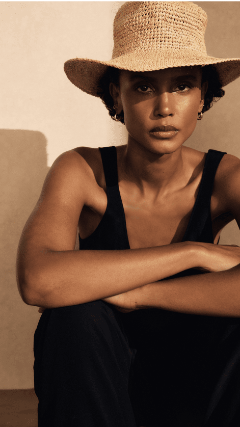 a woman in a hat sitting on a stool with her hands on her hips