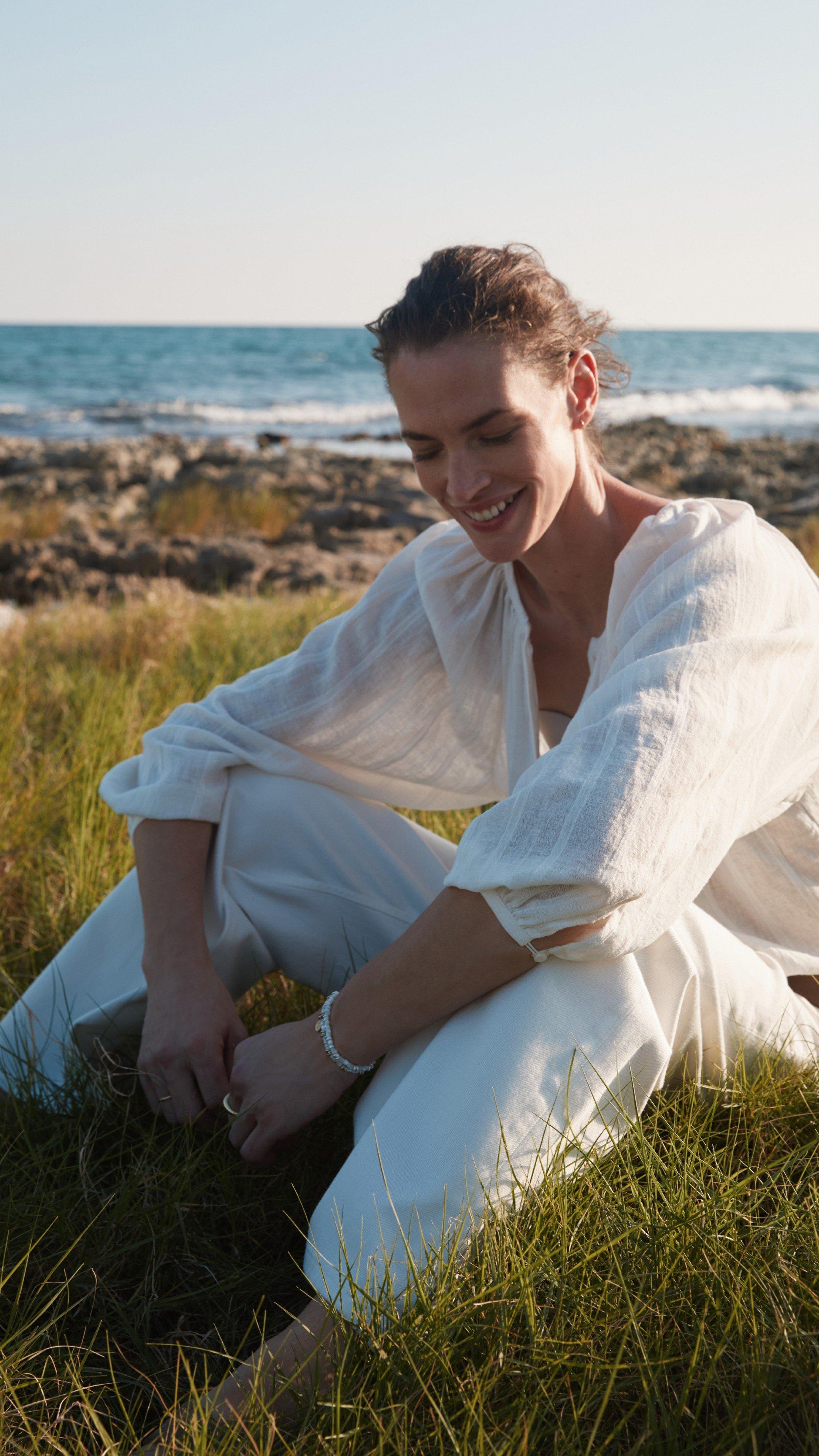 a woman sitting on the grass near the ocean with a cell phone