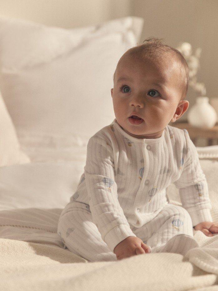 a baby in white pajamas sitting on a bed