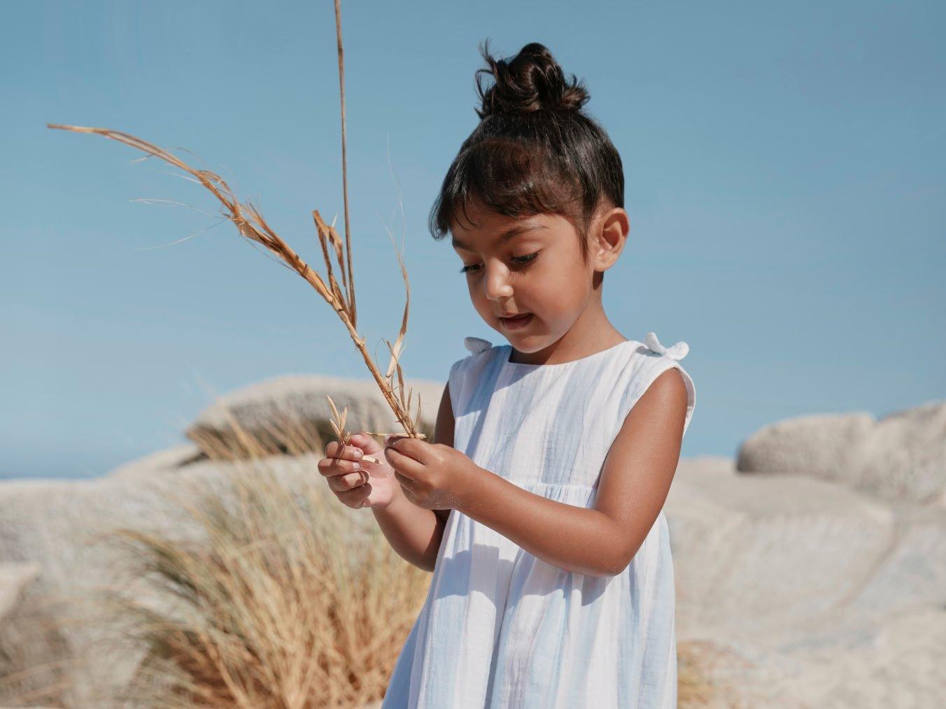 a little girl standing in the sand holding a plant