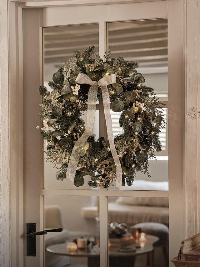 a wreath hanging from a door with a white bow