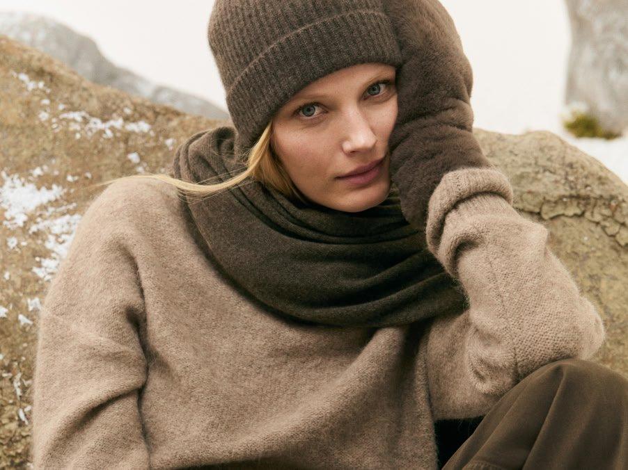 a woman in a hat and sweater sitting on a rock