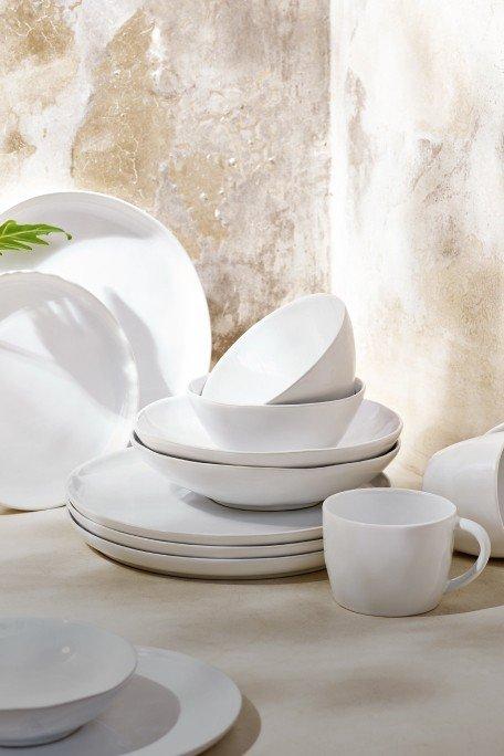 a pile of white dishes and cups on a table with a plant