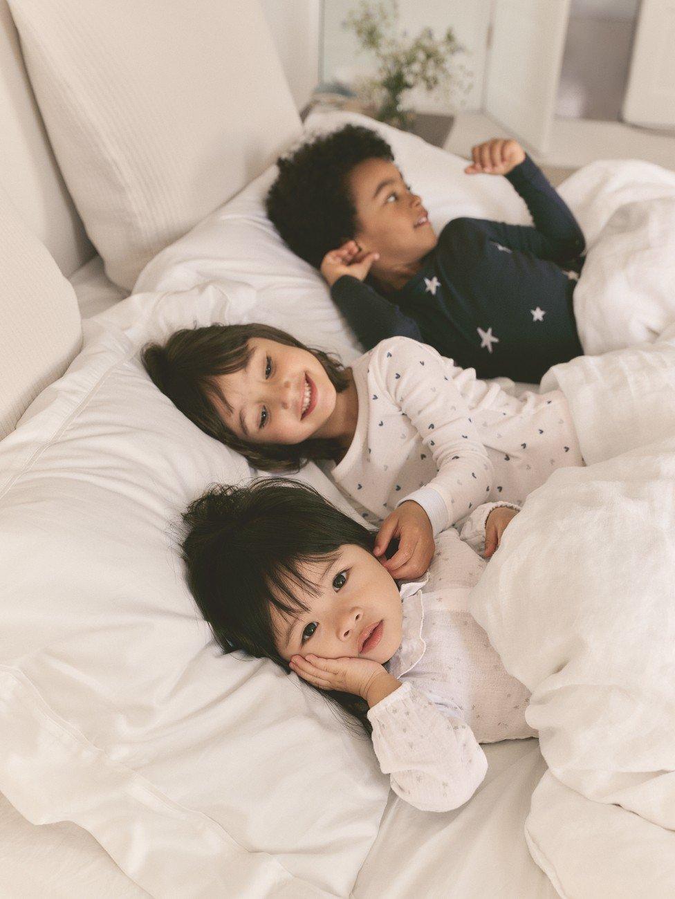 three children laying in a bed together with pillows