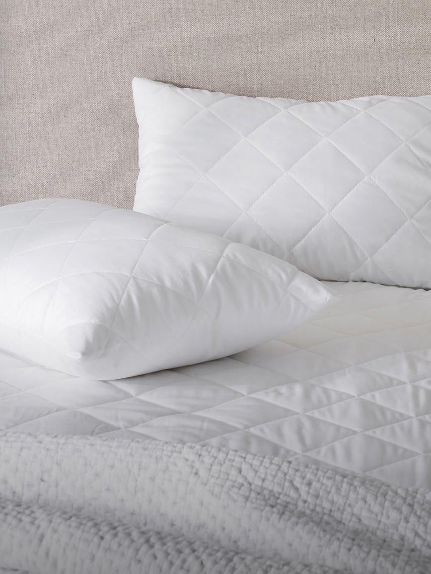 a bed with white sheets and pillows with a yellow pillow