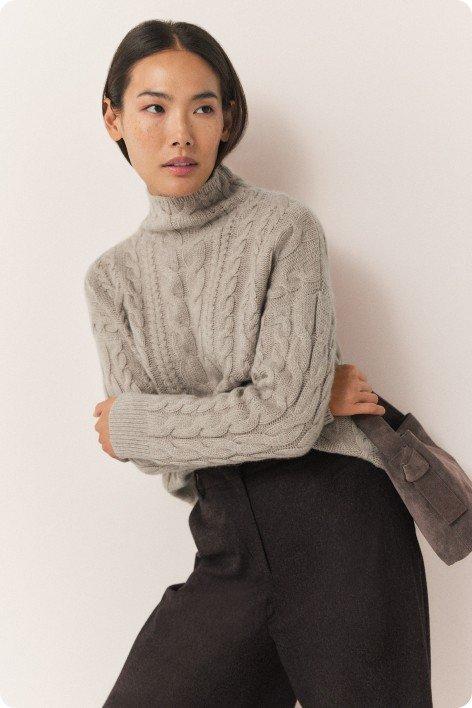 a woman in a grey sweater and black pants posing for a picture