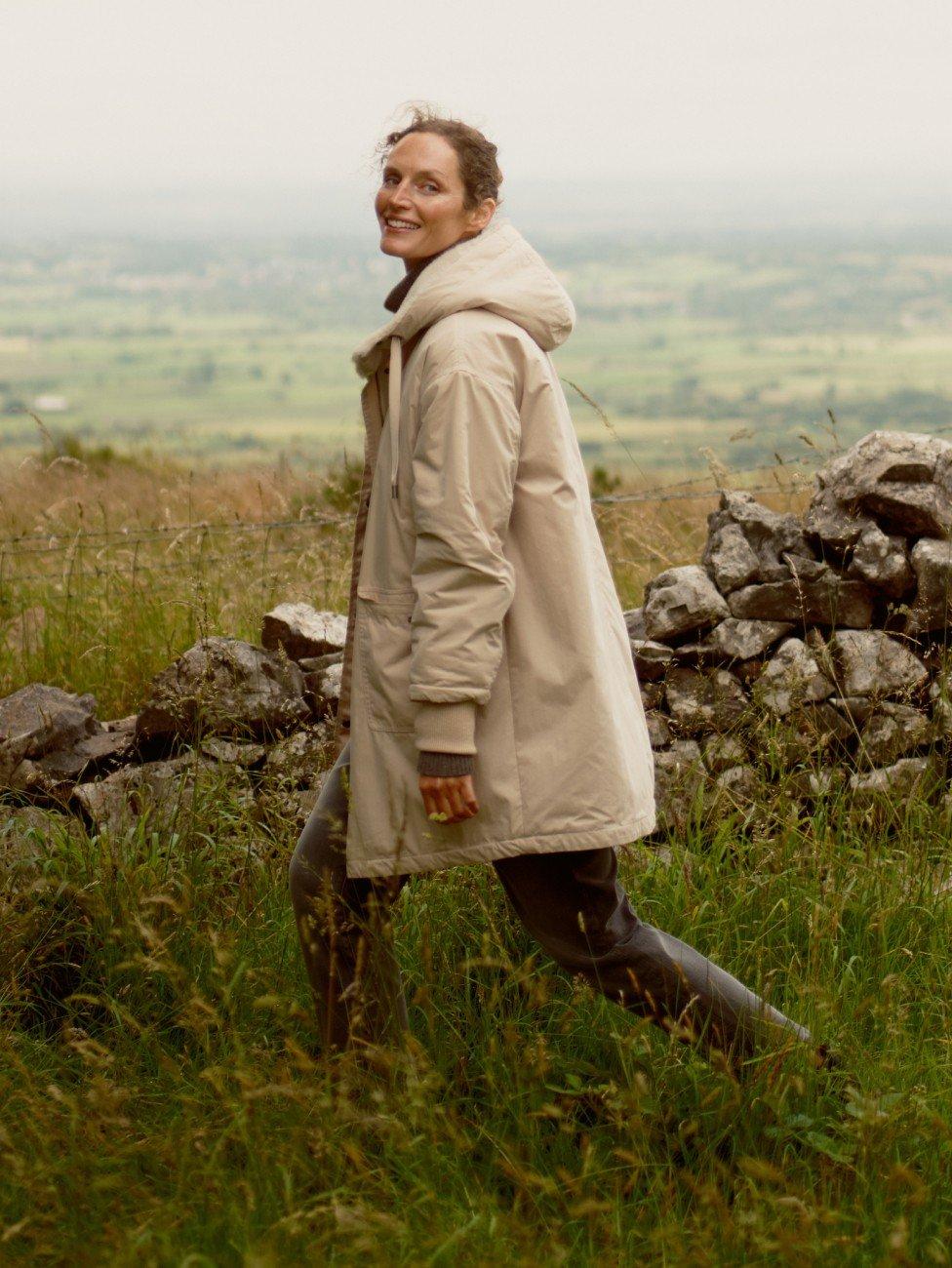 a woman in a brown sweater leaning against a wall