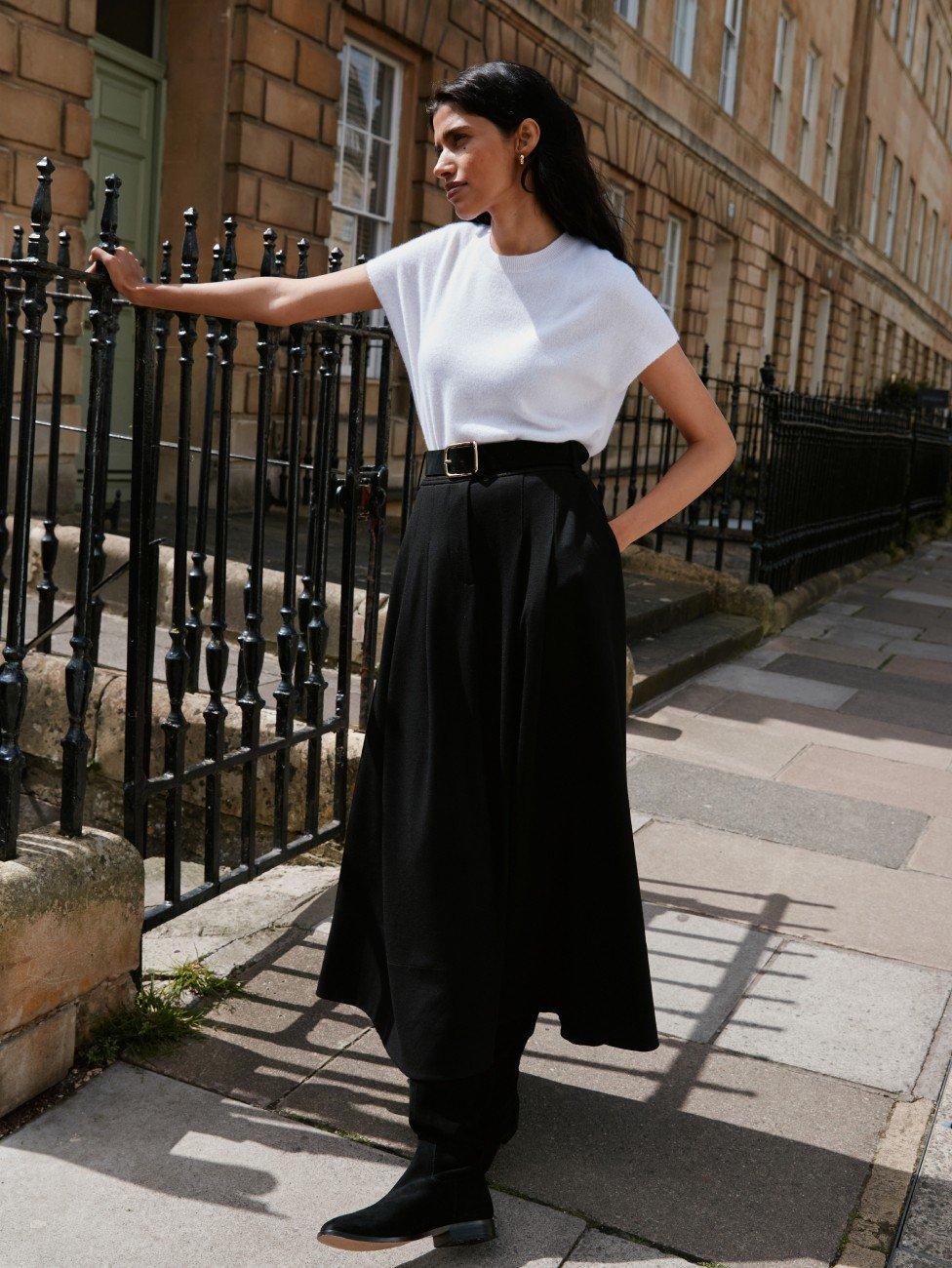 a woman in a white shirt and black skirt leaning against a fence